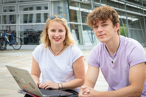 Studentin und Student vor einem Laptop auf den Stufen vor dem S-Bau. 