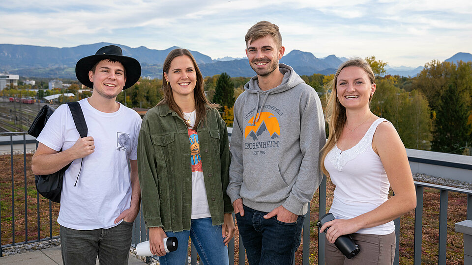 [Translate to English:] Vier fröhliche Studierende vor einem Bergpanorama.