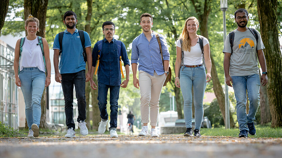 [Translate to English:] Eine Gruppe Studierender verschiedener Nationalitäten laufen nebeneinander unter einer Baumallee
